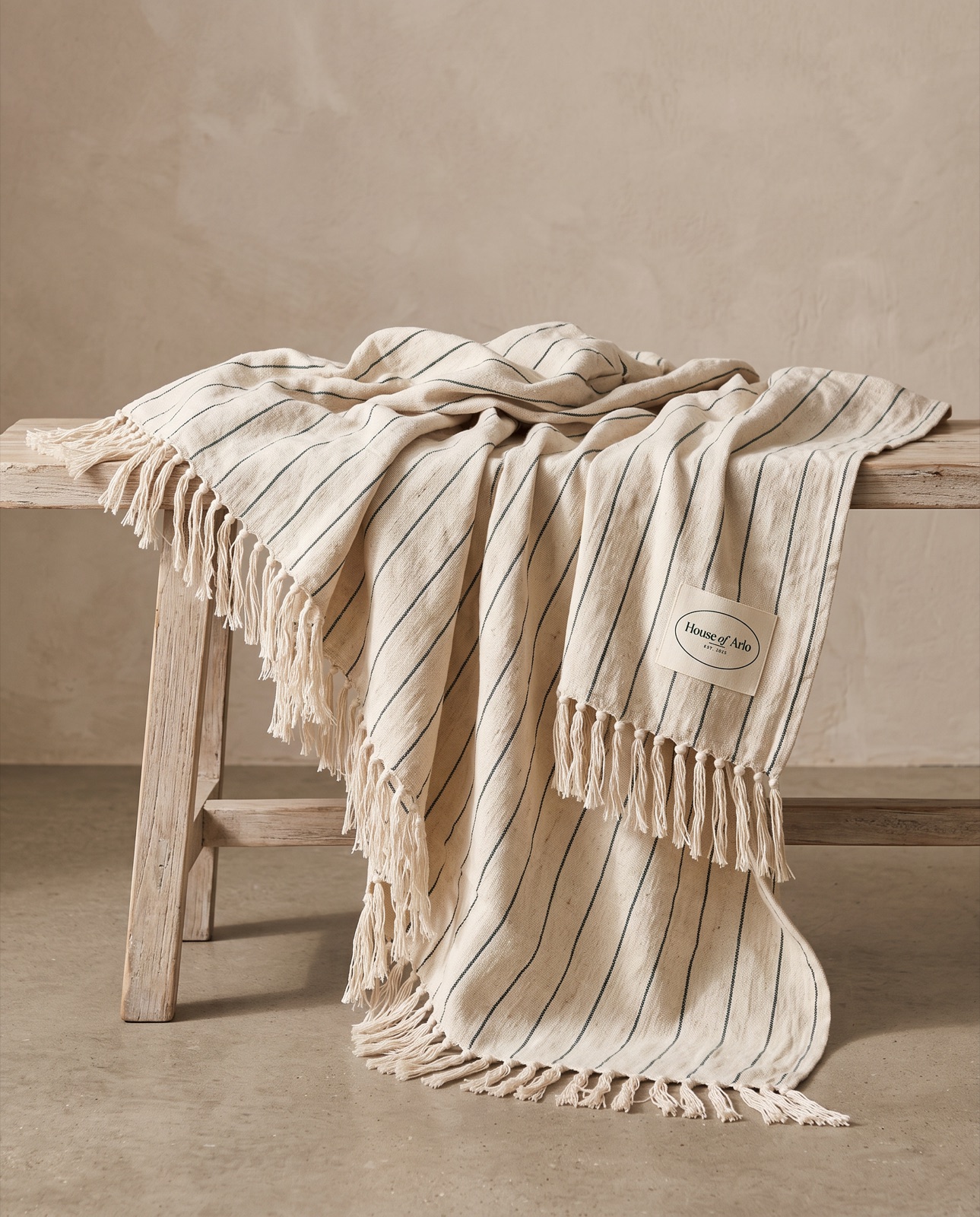 A cream linen tassel blanket draped over a timber bench