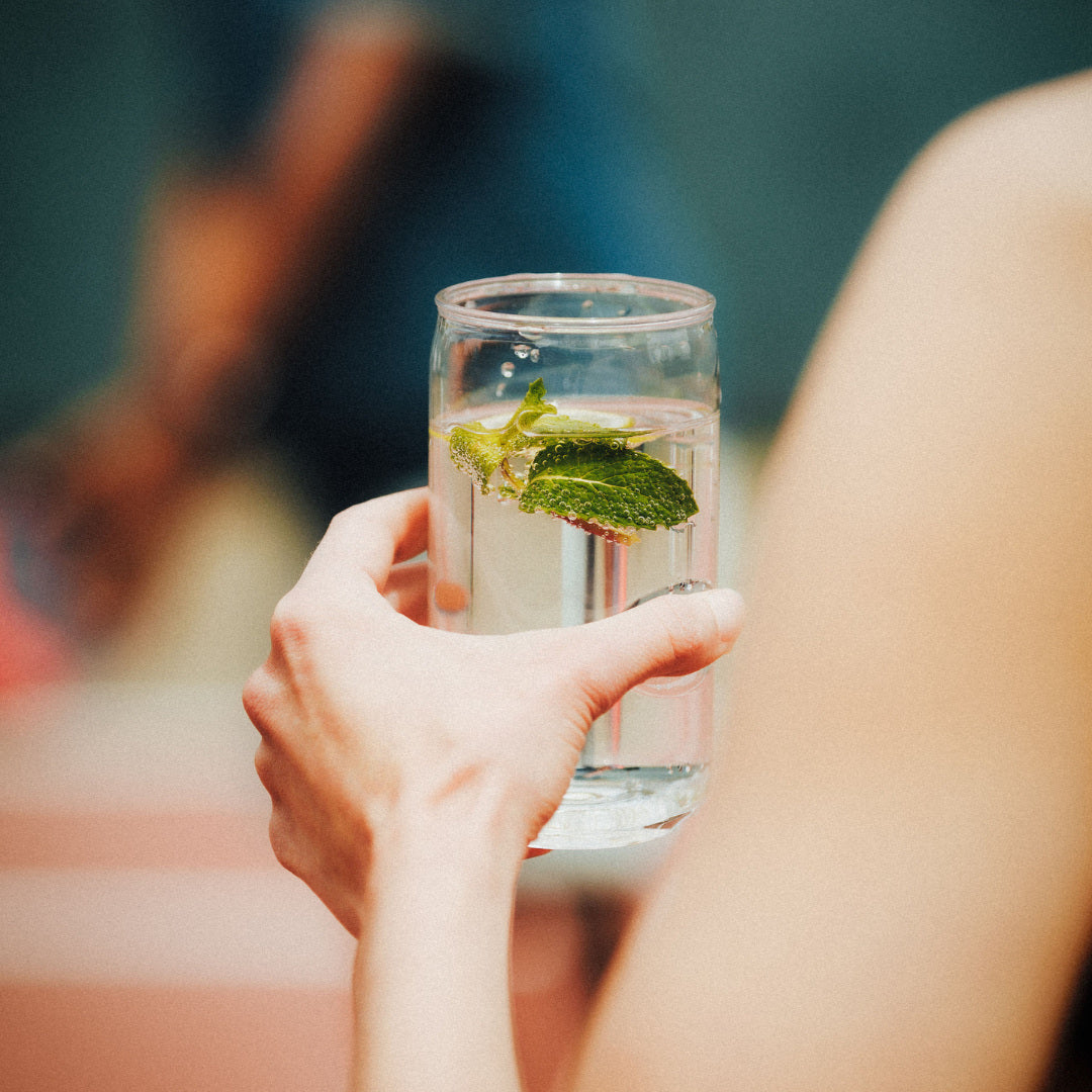 Govino can-shaped glass held with a clear drink and fresh mint