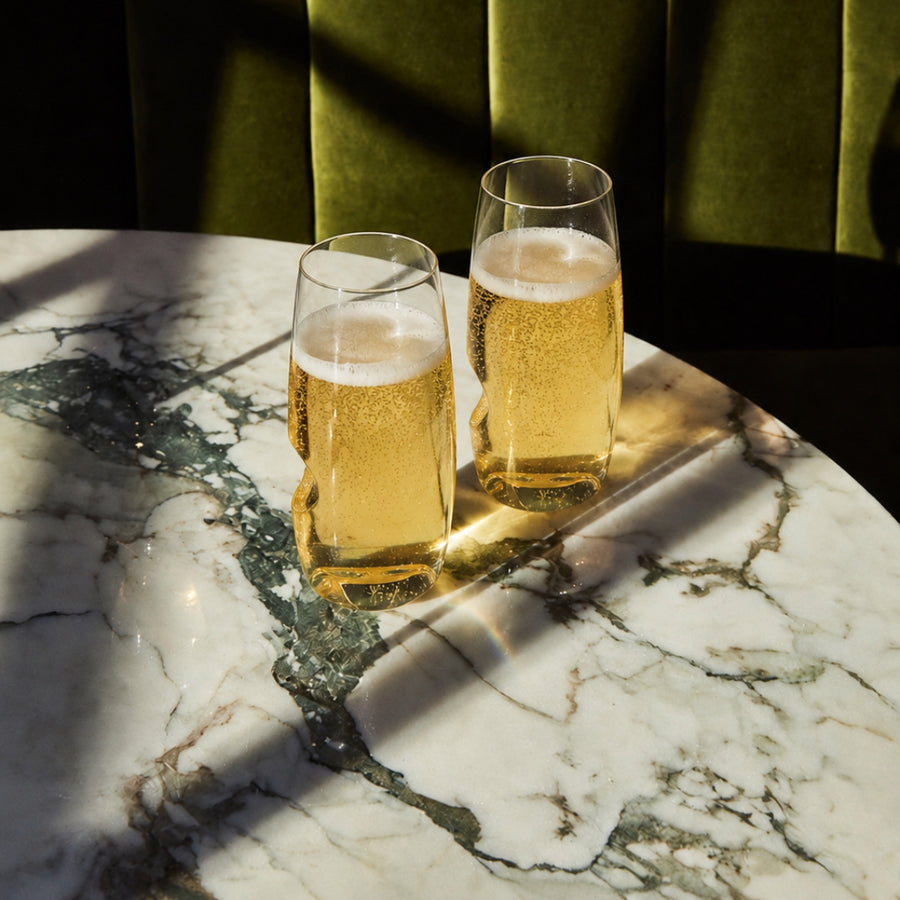Two Govino flute glasses with sparkling drinks on a sunlit marble table