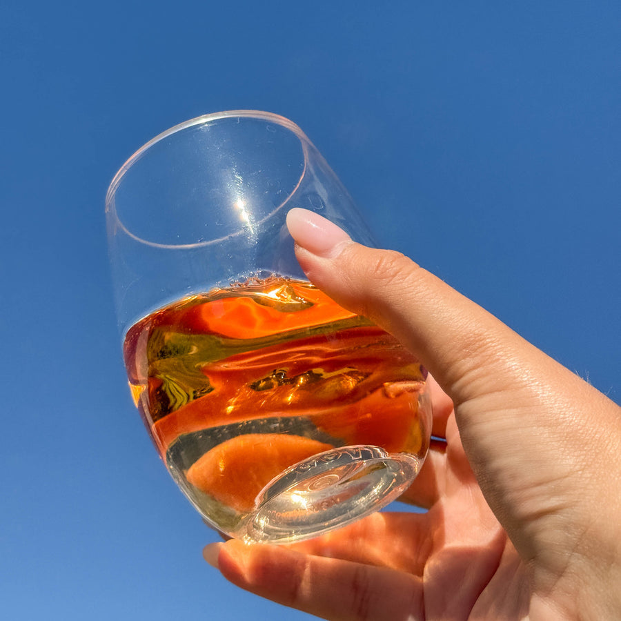 Govino wine glass held against a blue sky with an amber drink