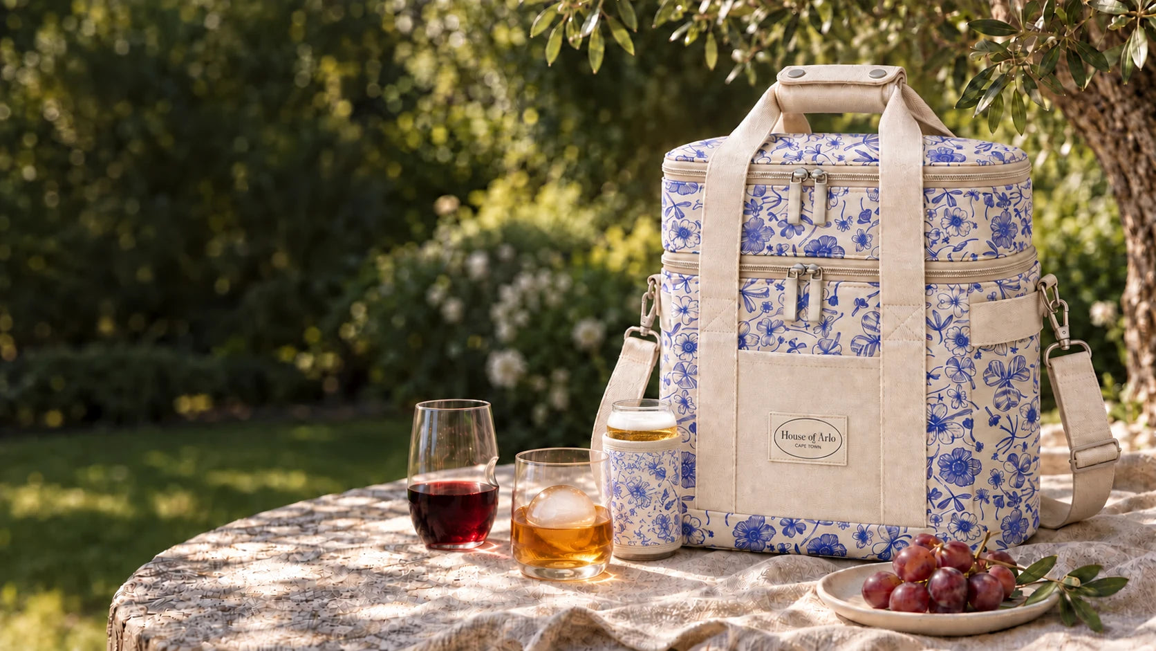 Blue botanical picnic bag with Govino drinkware and a matching can sleeve on a sunlit garden table
